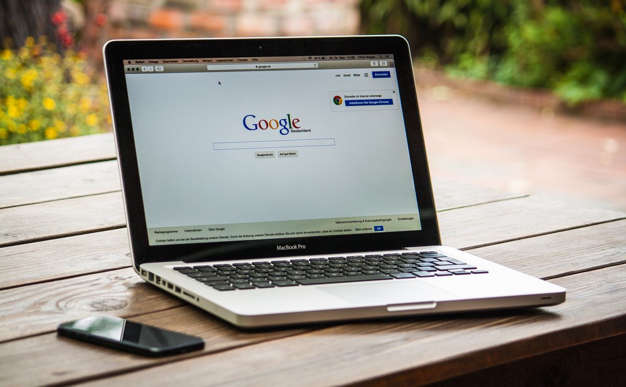 Un MacBook Pro affichant Google Search sur une table en bois, à l’extérieur, à côté d’un smartphone.